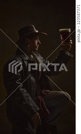 Cowboy raising pint of beer, admiring rich color and foam, dressed in classic western outfit with leather coat and hat Cowboy raising pint of beer, admiring rich color and foam, dressed in classic western outfit with leather coat and hat 123587371