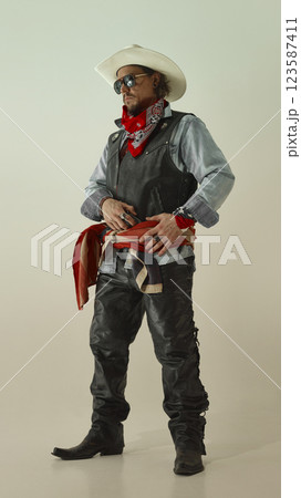 Confident man, cowboy in western outfit, gripping belt while looking to side, wearing white hat, sunglasses, and American flag Confident man, cowboy in western outfit, gripping belt while looking to side, wearing white hat, sunglasses, and American flag 123587411