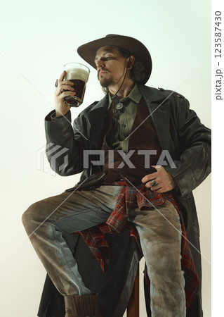 Handsome man, cowboy sitting on chair and enjoying cold foamy dark beer. Man wearing leather coat, worn jeans and shirt. 123587430