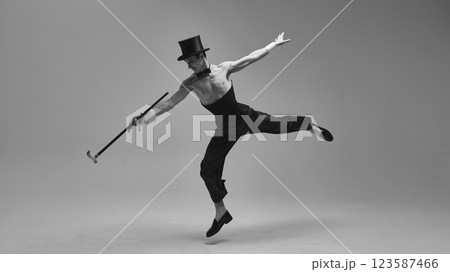 Dynamic performer in high-waisted corset and classic top hat jumping gracefully with expressive arms in monochrome photo filter. Concept of vintage time Dynamic performer in high-waisted corset and classic top hat jumping gracefully with expressive arms in monochrome photo filter. Concept of vintage time 123587466
