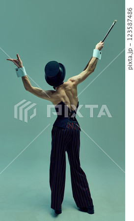 Rear view photo of performer in fitted corset and pinstriped trousers wielding cane with theatrical poise against green studio background. Rear view photo of performer in fitted corset and pinstriped trousers wielding cane with theatrical poise against green studio background. 123587486