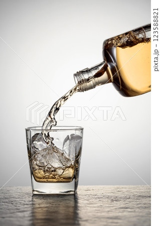 Whiskey is poured into a glass with ice. Whiskey is poured into a glass with ice. 123588821