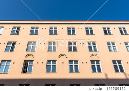 Symmetrical rows of windows decorate a light brown building against a bright blue sky in Helsinki. 123589152