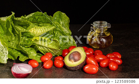 Vibrant still life composition of fresh tomatoes, onions, lettuce, and avocado on dark background 123589386