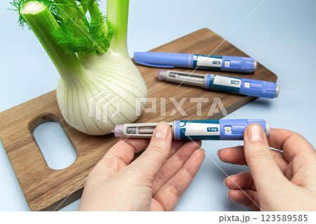 Hands holding Insulin injection pen and fennel vegetable root for diabetics and weight loss. 123589585