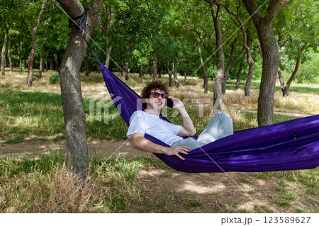 A young guy with curly hair is relaxing on a hammock on a hot summer day. 123589627