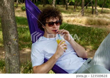 A young guy with curly hair is relaxing on a hammock on a hot summer day. 123589628