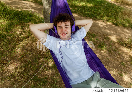 A young guy with curly hair is relaxing on a hammock on a hot summer day. 123589631