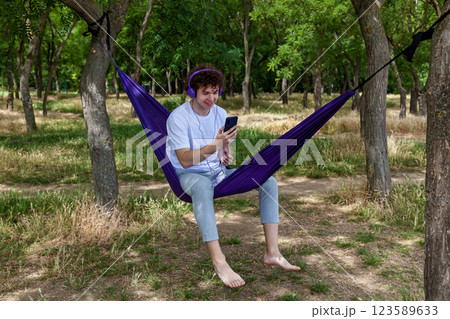 A young guy with curly hair is relaxing on a hammock on a hot summer day. 123589633