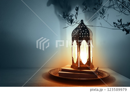 Moroccan, Arabic lantern on table glowing at night. Dark blue background. Silhouette of olive tree branches. Greeting card for Muslim holy month Ramadan Kareem, Eid Mubarak. Festive background. 123589979