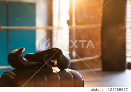 Boxing gloves lying down on boxing ring in empty gym. Equipment for fight training competition black protective boxing gloves ready for fighter winner on ring. Strength fit body workout training 123589987