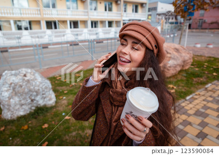 Top view of young pretty Caucasian happy woman in a coat and hat holds cup of coffee call on smartphone in city street. Lifestyle and city life 123590084