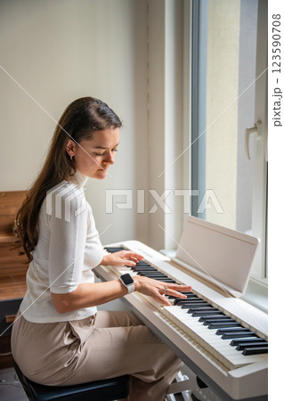 Young woman playing on white piano synthesizer at home. Concept of home lesson of music: learning music enhances motor skills, hearing, and intelligence, fostering creativity 123590708