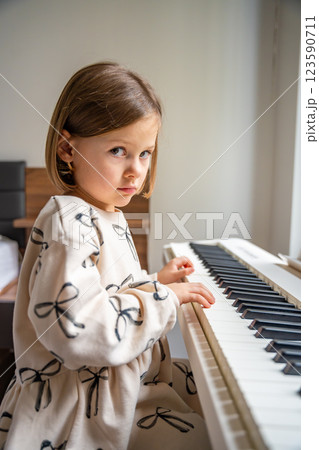 Home lesson on music for the girl on white piano synthesizer. Concept of early development: learning music enhances motor skills, hearing, and intelligence, fostering creativity from childhood 123590711