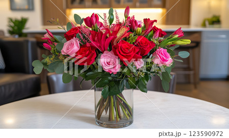 Elegant bouquet with vibrant red and pink roses in glass vase on a table with blurred kitchen background 123590972
