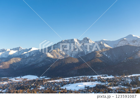 Stunning winter landscape of Zakopane, Poland, featuring the snow-covered Tatra Mountains at sunset. The picturesque alpine town, surrounded by forests and peaks, offers breathtaking views and is a po 123591087