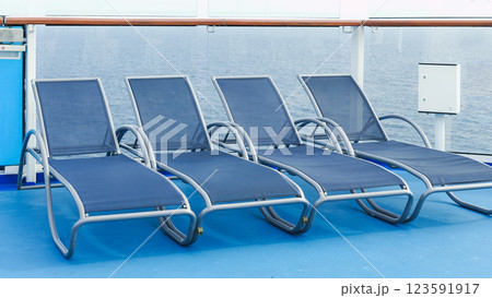 A serene view of blue deck chairs perfectly arranged in neat rows on a luxurious cruise ship deck. A serene view of blue deck chairs perfectly arranged in neat rows on a luxurious cruise ship deck. 123591917