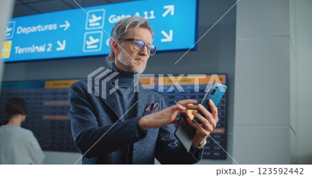 Airport Terminal: Mature Man Scanning Plane Ticket Using Smartphone to Check Flight Information Airport Terminal: Mature Man Scanning Plane Ticket Using Smartphone to Check Flight Information 123592442