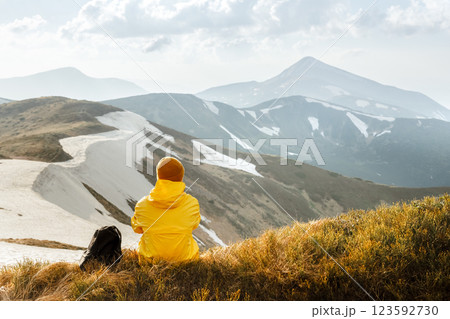A tourist in yellow jacket sits on the edge of a mountain 123592730