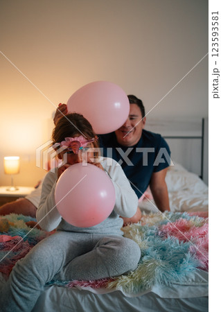 Family fun: young caucasian girl and adult hispanic male playing with balloons on bed 123593581