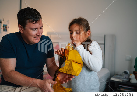 Caucasian adult male and child blowing balloon indoors 123593582
