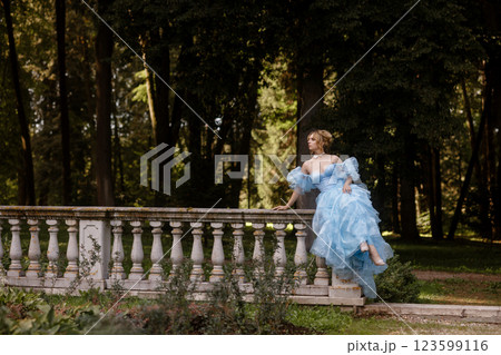 Romantic Woman in a Light Blue Gown Posing on a stone balustrade in a picturesque garden. 123599116