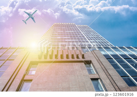 A modern office skyscraper and a white passenger airliner flying over this building A modern office skyscraper and a white passenger airliner flying over this building 123601916
