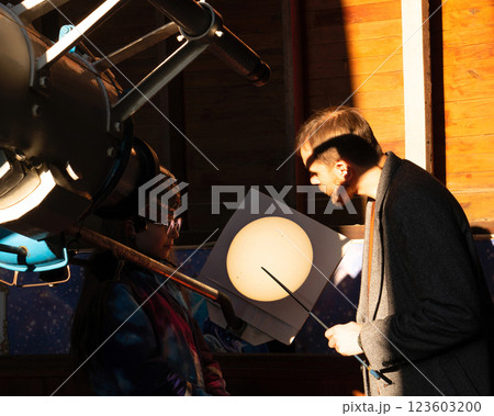 Man and girl examine projected solar image from telescope. Man and girl examine projected solar image from telescope. 123603200