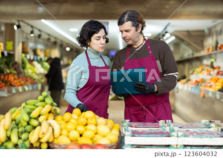 Man and woman store employee with folder of documents takes inventory in vegetable store Man and woman store employee with folder of documents takes inventory in vegetable store 123604032
