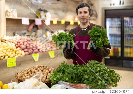Adult man seller puts bunches of parsley on display Adult man seller puts bunches of parsley on display 123604074