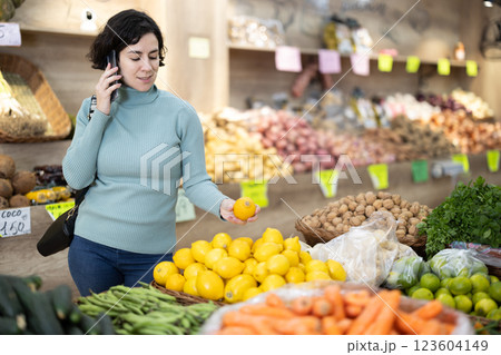 Woman talks on a mobile phone while shopping for fruits and vegetables in grocery supermarket 123604149