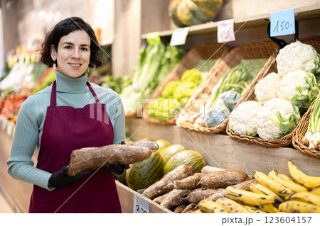 Adult woman seller with cassava in vegetable shop Adult woman seller with cassava in vegetable shop 123604157