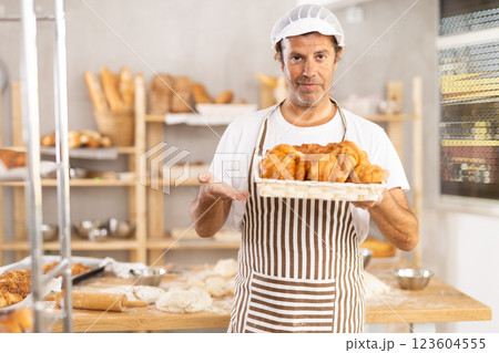Caucasian male cook-baker worker with basket of croissant, shows many products 123604555