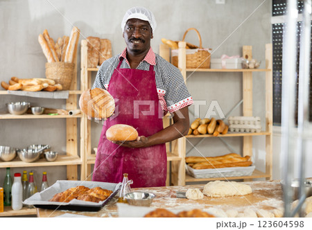 Male baker with basket of baked goods behind bakery counter inviting to buy bread 123604598