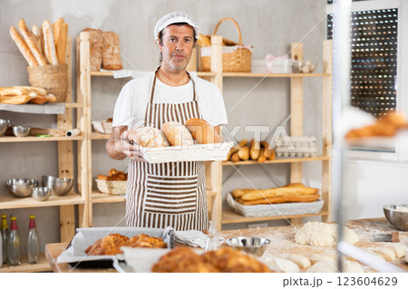 Caucasian male cook-baker worker with loafs of bread, shows many products Caucasian male cook-baker worker with loafs of bread, shows many products 123604629