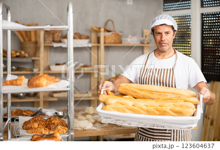 Smiling male salesman showing assortment of bakery products behind bakery counter Smiling male salesman showing assortment of bakery products behind bakery counter 123604637