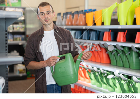 Young man chooses watering can in store Young man chooses watering can in store 123604655