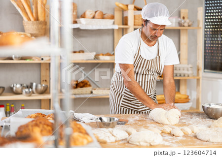 Male baker in uniform prepares raw dough, kneads it with his hands 123604714