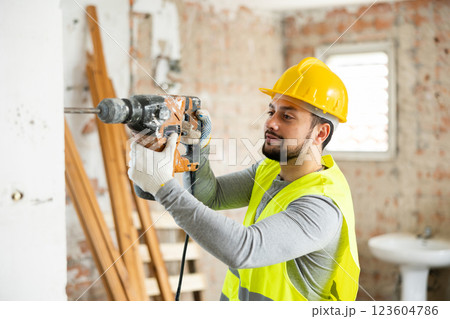Professional builder drilling hole in wall with perforator in repairable room 123604786
