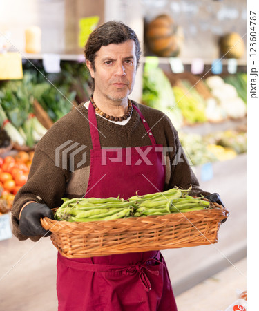Adult man seller with basket of green peas Adult man seller with basket of green peas 123604787