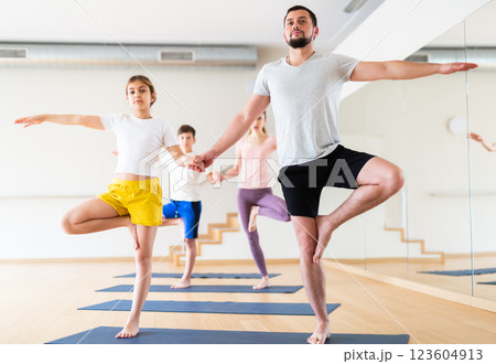 Young girl standing in tree pose with her father during yoga training 123604913