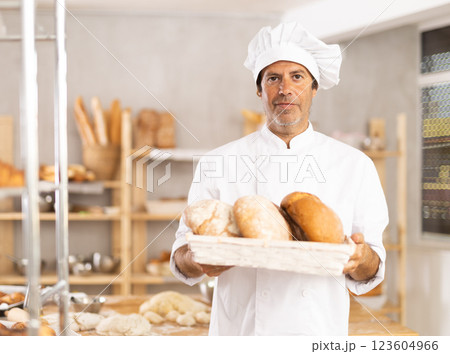 Caucasian male cook-baker worker with loafs of bread, shows many products Caucasian male cook-baker worker with loafs of bread, shows many products 123604966