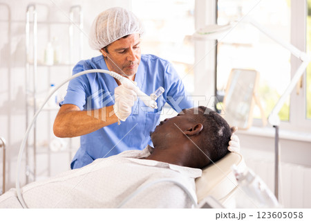 Aesthetician applying atomized nutrients onto black man face 123605058