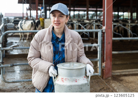 Milkmaid with aluminium cans near open cowshed at dairy farm 123605125