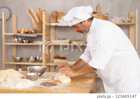 Caucasian guy works in bakery as baker, kneads dough, works with flour. 123605147