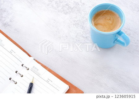 ミルクをたっぷり入れたコーヒー、カフェ・ラッテを飲みながら、システム手帳でデスクワーク中のイメージ ミルクをたっぷり入れたコーヒー、カフェ・ラッテを飲みながら、システム手帳でデスクワーク中のイメージ 123605915