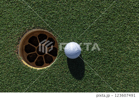 In the hole, White golf ball on green grass with golf hole, Golf ball ready to be shot, Golf ball close up on green grass in the hole, Top view. In the hole, White golf ball on green grass with golf hole, Golf ball ready to be shot, Golf ball close up on green grass in the hole, Top view. 123607491