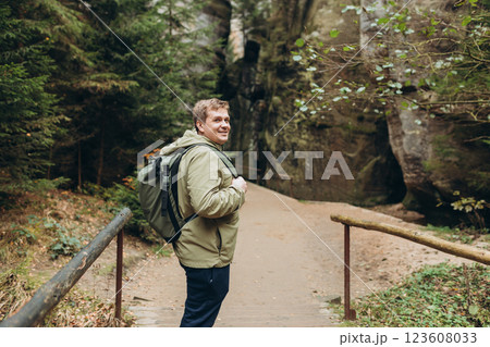 A tourist with a backpack stands against the background of a mountains and forest. Young 30s blonde man hiking in nature. Travel, adventure. Concept of an active lifestyle. High quality photo. A tourist with a backpack stands against the background of a mountains and forest. Young 30s blonde man hiking in nature. Travel, adventure. Concept of an active lifestyle. High quality photo. 123608033