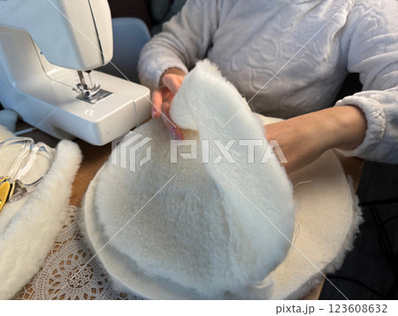 A woman is working at a sewing machine. She is sewing a pet bed from fur fabric. She is sewing the bottom of the bed. Oblique Angle. A woman is working at a sewing machine. She is sewing a pet bed from fur fabric. She is sewing the bottom of the bed. Oblique Angle. 123608632