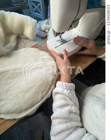 A woman is working at a sewing machine. She is sewing a pet bed from fur fabric. She is sewing the bottom of the bed. Oblique Angle. A woman is working at a sewing machine. She is sewing a pet bed from fur fabric. She is sewing the bottom of the bed. Oblique Angle. 123608633